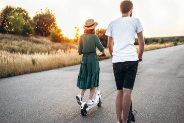 Mobiletlerle yürüyen mutlu çift. Elbise ve şapka giymiş genç bir kadın.