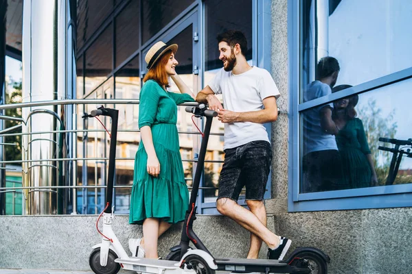 Una giovane donna in abito e uomo parlando tra loro e godere di un modo conveniente per viaggiare in città su scooter elettrici — Foto Stock