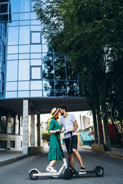 Una giovane donna e un uomo godono di una passeggiata in città su scooter elettrici. Tecnologie dei contenuti. Coppia parlare e divertirsi — Foto Stock