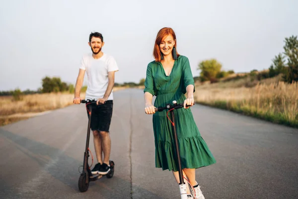 Jong vrolijk glimlachend stel dat plezier beleeft aan het rijden van elektrische scooter op de weg op het platteland. Contenttechnologieën — Stockfoto