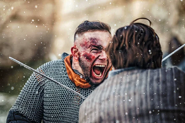 Two warriors in armor with weapons fighting with swords. Close up of emotions on the face of a warrior smeared with blood — Stock Photo, Image