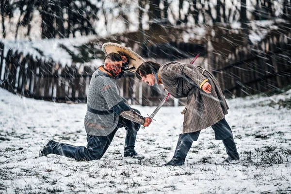 The process of a medieval battle in the snow. A soldier in armor kills an enemy with a sword — 스톡 사진