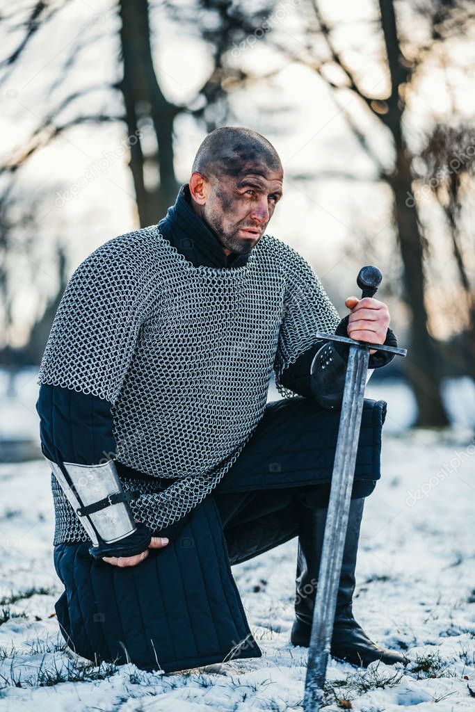 A medieval warrior in chain mail armor kneeling with his sword i