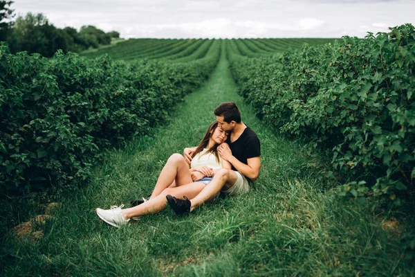 Woman with long hair and man sitting between currant bushes, hug — 스톡 사진