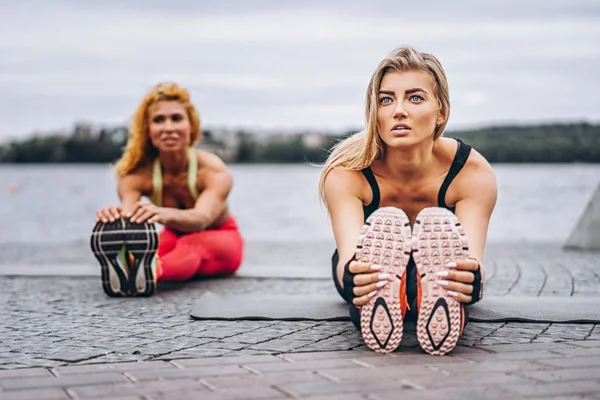 Дві жінки практикують вправи йоги на килимку на вулиці поруч з — стокове фото