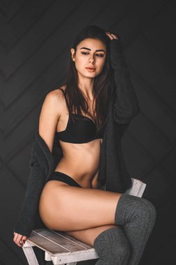 Siyah iç çamaşırlı genç esmer, dizlik ve hırka örüyor.