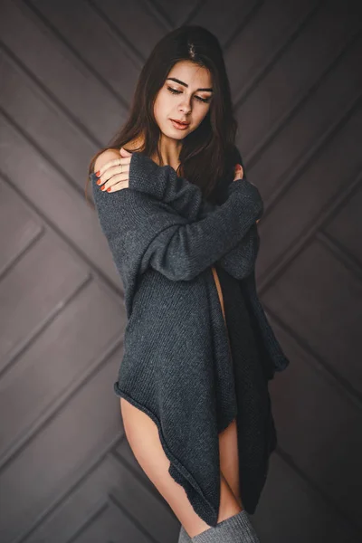 Nudo giovane donna bruna con i capelli lunghi è avvolto in un cardigan grigio su uno sfondo scuro monocromatico — Foto Stock