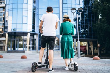 Siyah beyaz elektrikli scooterlı bir adam ve kadın. Arkadan bak. C