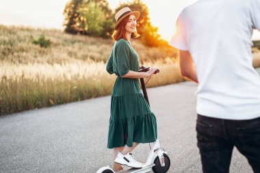 Mobiletlerle yürüyen mutlu çift. Elbise ve şapka giymiş genç bir kadın.