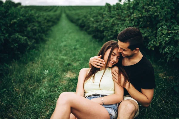 Donna con i capelli lunghi e l'uomo seduto tra cespugli di ribes, abbraccio — Foto Stock