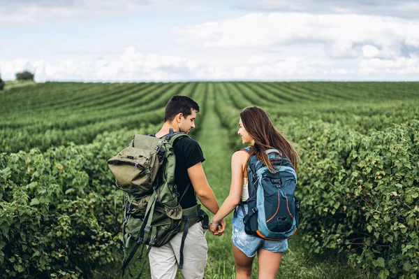 Vista posterior de pareja joven con mochilas en plantaciones de grosella — Foto de Stock