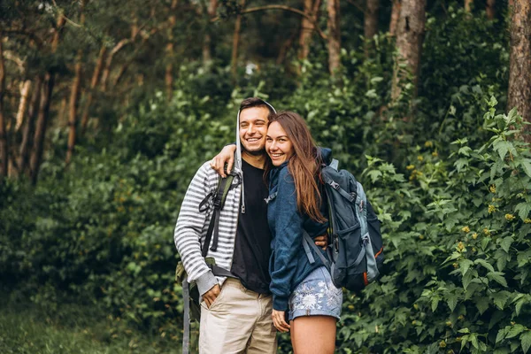 Unga par med ryggsäckar på ryggen ler och går i skogen, njuta av promenaden — Stockfoto