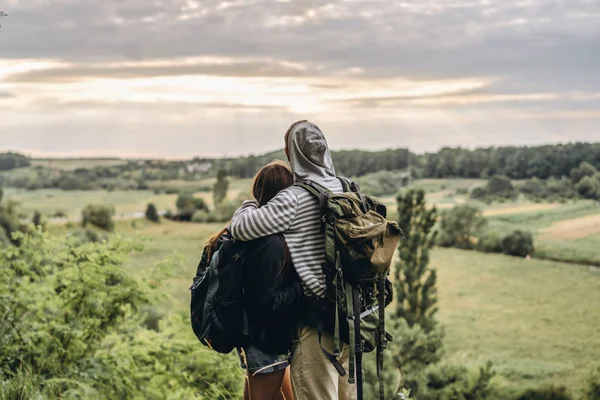 Achteraanzicht van jong stel met rugzakken. Man en vrouw omarmd en kijkend naar het landschap — Stockfoto