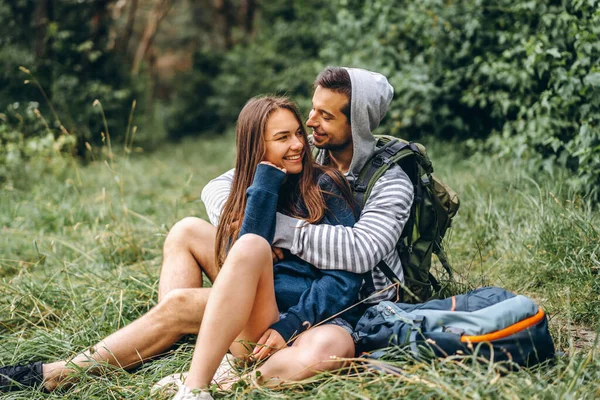Žena s dlouhými vlasy a muž sedí na trávě v lese — Stock fotografie