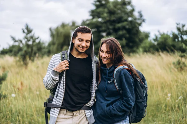 Jovem casal amoroso com mochilas andando e gentilmente abraçando — Fotografia de Stock