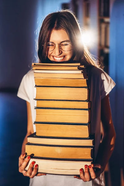 Студент молодої дівчини в окулярах в бібліотеці посміхається і несе стопки книг. Підготовка до іспиту — стокове фото