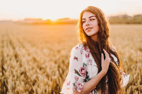 一个有着长长的卷发和雀斑脸的令人难以置信的年轻女人 日落时穿着衣服站在麦田里的女人 近景肖像 — 图库照片