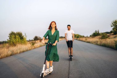 Genç ve mutlu bir çift kırsalda elektrikli scooter sürerken eğleniyor. İçerik teknolojileri.