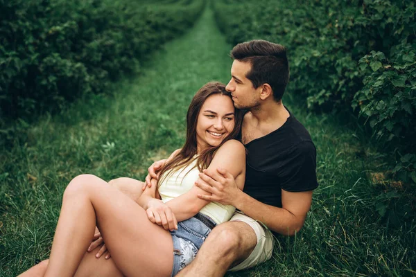 长发女人和男人坐在醋栗丛中 拥抱和亲吻 绿醋栗种植园的背景 — 图库照片