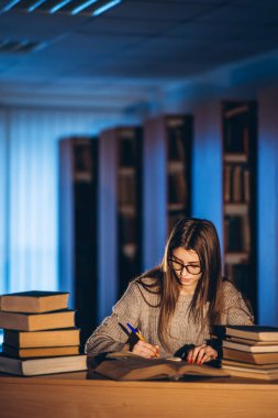 Gözlüklü genç öğrenci sınava hazırlanıyor. Akşamları kütüphanedeki masada bir yığın kitapla oturan bir kız..
