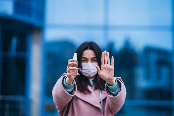 Close up hands of female in medical mask cleaning her hands with sanitizer outdoor in the city to prevent virus deseases. Coronavirus, COVID-19, epidemic, pandemic, quarantine concept