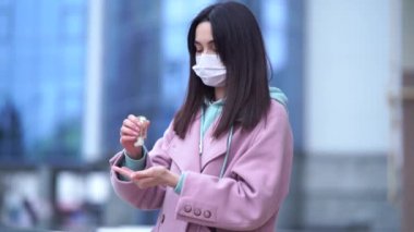 Tıbbi maskeli bir kadının ellerini şehirde virüs hastalıklarını önlemek için jel dezenfektanla temizleyin. Coronavirus, COVID-19, salgın, salgın, karantina konsepti