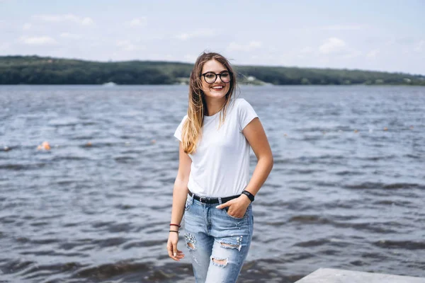 スタイリッシュなメガネで美しい若い女性の肖像画 湖の風景の背景にポーズ白いTシャツの女の子 — ストック写真