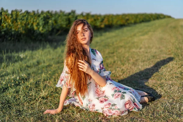 美丽女人的全长肖像 卷曲的长发 背景为醋栗原野 阳光明媚的日子 穿着浅色衣服的女孩坐在草地上 — 图库照片