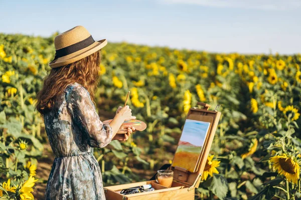 一个头发卷曲 头戴帽子的年轻女子正在画大自然 美丽的一天 一个女人站在向日葵地里 — 图库照片