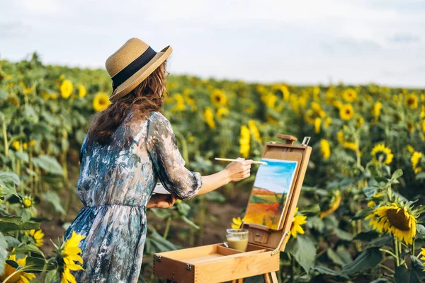 一个头发卷曲 头戴帽子的年轻女子正在画大自然 美丽的一天 一个女人站在向日葵地里 — 图库照片
