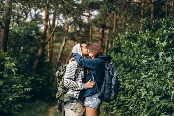 在森林里背着背包的年轻夫妇 有爱心的男人在树林里散步的时候吻了他美丽的女朋友 — 图库照片