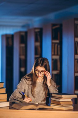 Gözlüklü genç öğrenci sınava hazırlanıyor. Akşamları kütüphanedeki masada bir yığın kitapla oturan bir kız..