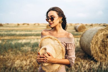 Buğday tarlasında ve saman balyalarında çıplak omuzlu, güneş gözlüklü gülümseyen kadın..