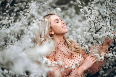 Muhteşem gülüşlü bir kadın çiçek açan bahçede eğleniyor. Doğal arka planda kırmızı elbiseli bir kadın, sağIık ve sakin bir konsept. Parkta kıvırcık sarı saçlı, şehvetli sarışın kız.