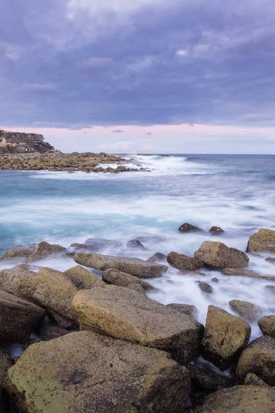 オーストラリアの海岸線の長い露出写真 波は研磨された岩の上を流れている 空は穏やかな色をしている — ストック写真