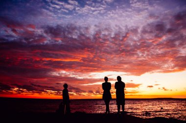Üç arkadaşın siluetleri bulutlarla ve renklerle dolu inanılmaz ve canlı bir günbatımına bakıyor..