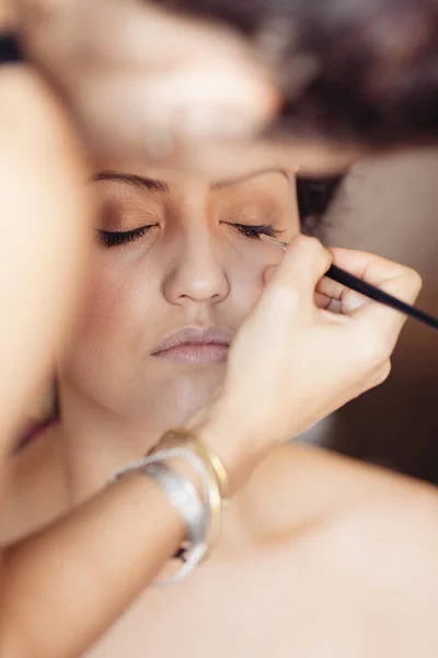 Head shot of  beautiful woman having cosmetics applied above eyelids by a makeup artist.