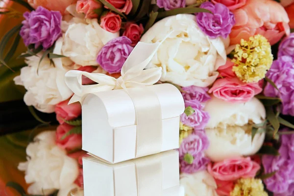 Geschenkbox auf einem Hintergrund eines Blumenstraußes — Stockfoto