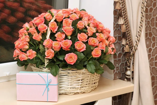 No peitoril da janela está uma grande cesta de rosas e uma caixa de presente . — Fotografia de Stock