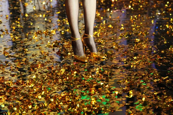 Pernas femininas em meias meia-calça em sapatos de ouro em um chão de ouro fro — Fotografia de Stock