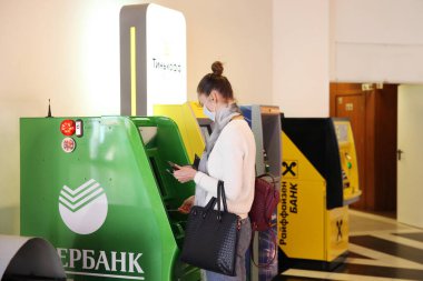 Sberbank ATM 'nin yanında maske takan genç bir kadın. Moskova. 27.03.2020