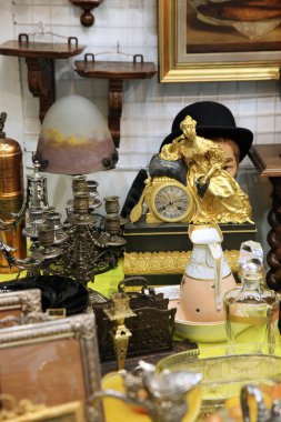 Altın bir kadın heykeli, şapka ve bit pazarındaki diğer eşyaların olduğu klasik saat.