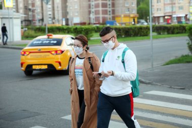 Yüzlerinde gözlüklü ve tıbbi maskeleri olan gençler caddede bir taksinin arka planına karşı karşıya geliyorlar. Moscow.11.05.2020
