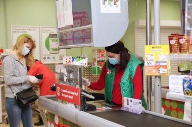 Müşteri ve tıbbi maskeli ve eldivenli bir satıcı Pyaterochka süpermarketinin kasasında. Moscow.11.05.2020