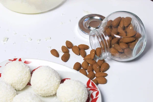Příprava Raffaello sladkosti doma. Hotové cukroví leží na talíři. Na pozadí sklenici s rozptýlenými mandle. — Stock fotografie