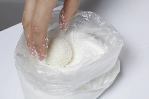 Preparação de doces Raffaello em casa. Uma mulher rola uma bola de uma mistura de leite condensado e chips de coco . — Fotografia de Stock