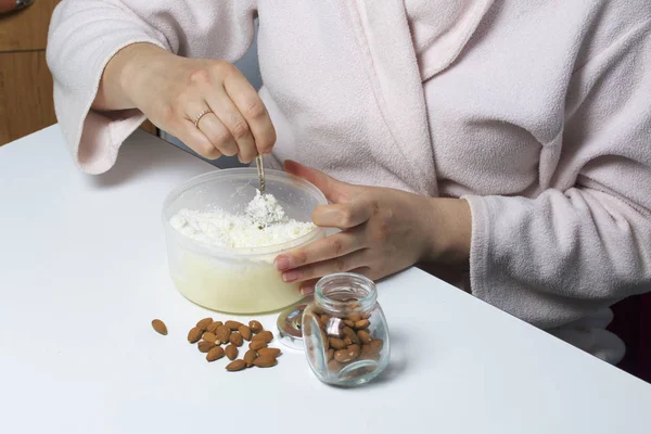 Walnut almonds. In a glass jar, scattered on the table. Near the container in which the woman is mixing coconut shavings with condensed milk. On a white background.
