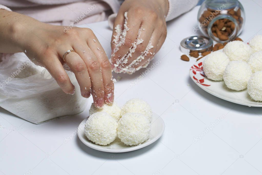 Preparation of Raffaello sweets at home. A woman rolls a ball from a mixture of condensed milk and coconut chips.
