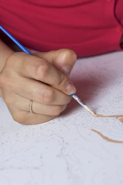 Art. Tekening van getallen. Een vrouw schildert een doek van katoen. Maakt gebruik van penselen, verven en water genummerd in een glas. — Stockfoto