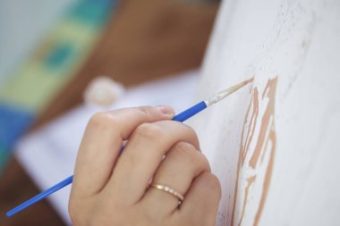 Sanat. Sayılarla çizim. Bir kadın bir tuval pamuk boyar. Fırçalar, boyalar ve su bir bardak sayılı kullanır.